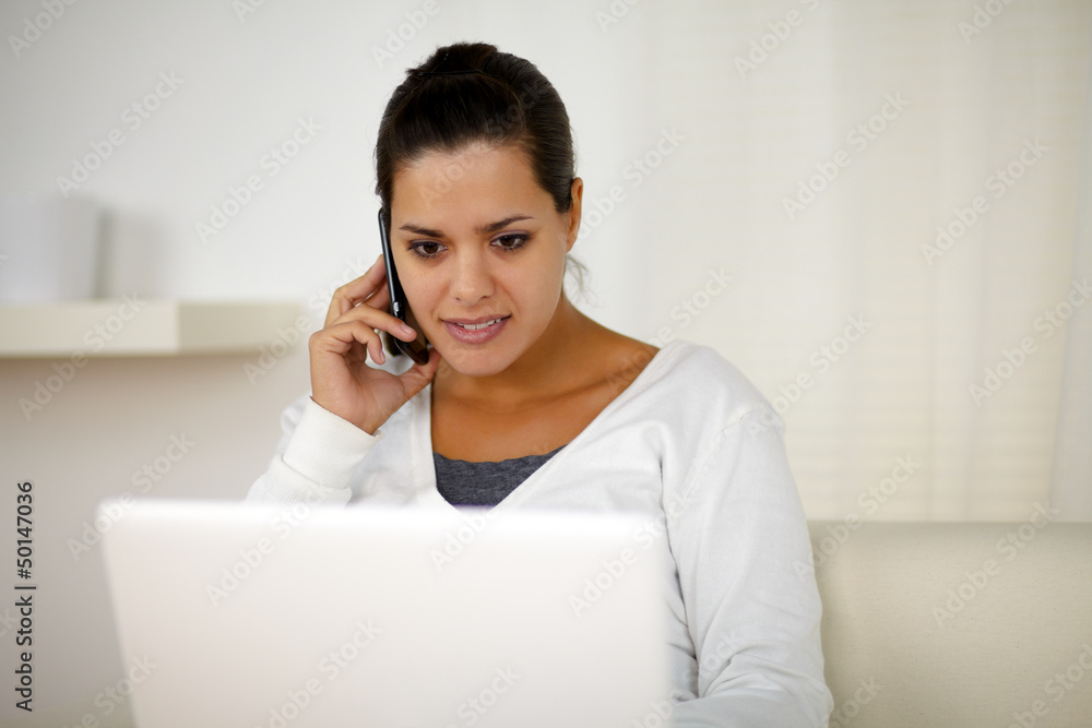 Female conversing on cellphone in front of laptop Female conversing on cellphone in front of laptop