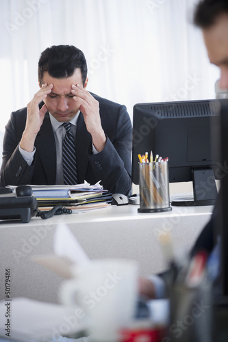 Mixed race businessman rubbing head at desk