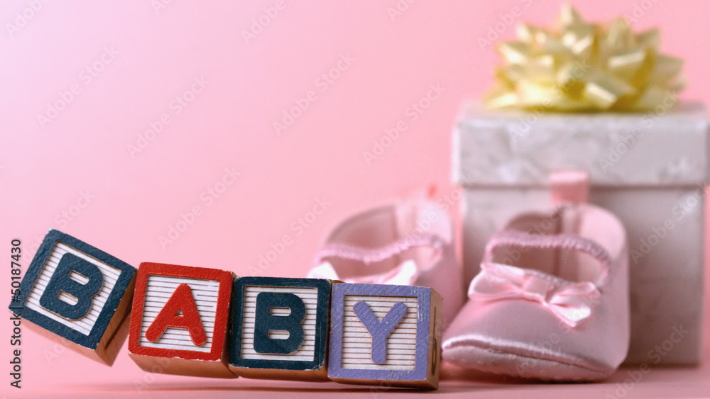 Baby blocks toppling over in front of booties and gift box Baby blocks toppling over in front of booties and gift box
