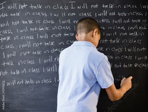 Hispanic boy writing punishment on blackboard photo