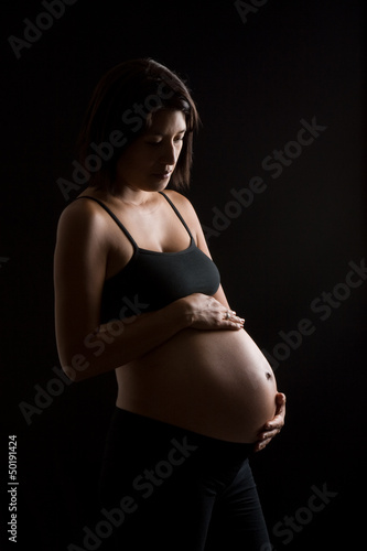 Pregnant Peruvian woman touching her belly against black backgro