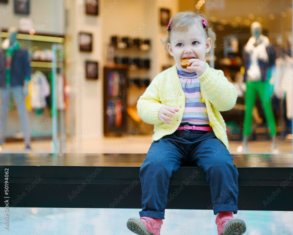 Cute little girl eating biscuit cake on bench