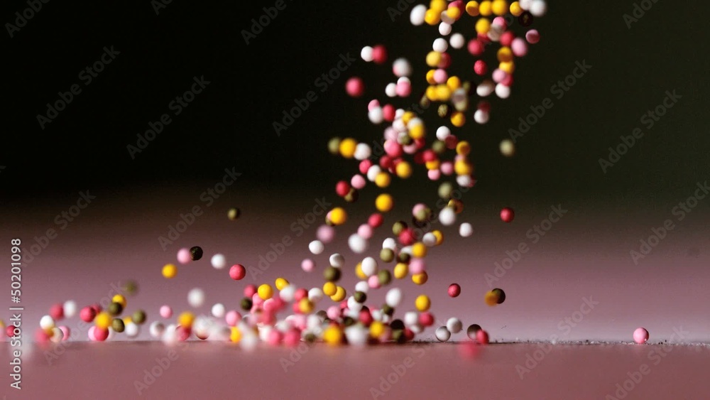 Sprinkles pouring onto pink surface on black background Sprinkles pouring onto pink surface on black background