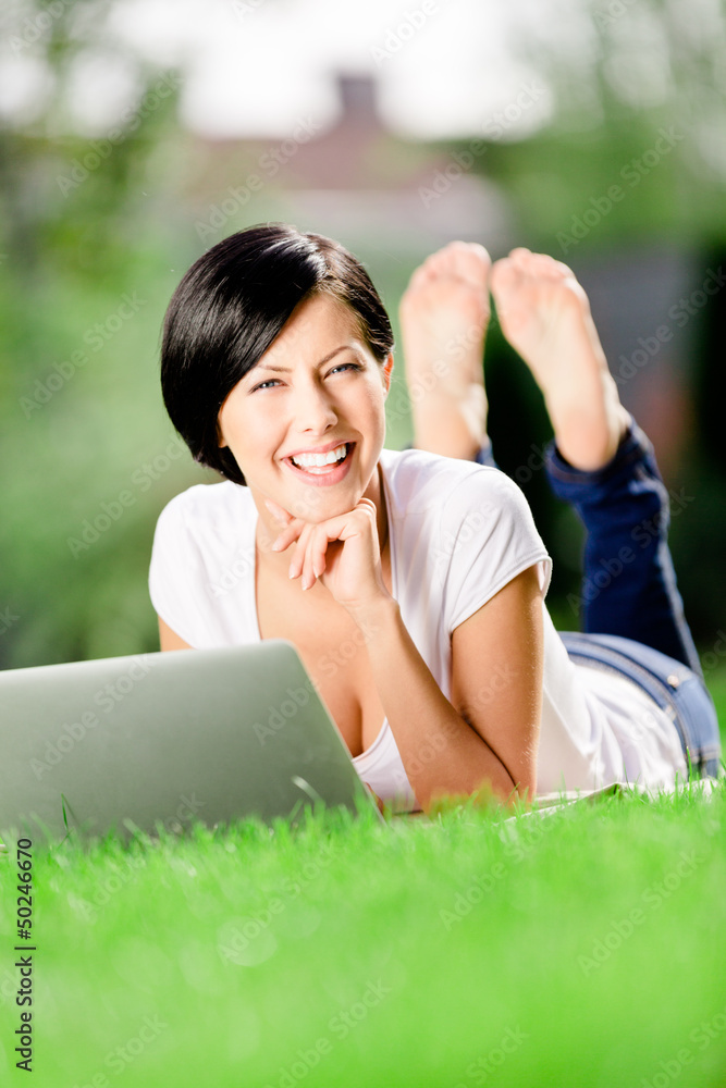 Girl lying on the grass works at the silver pc Girl lying on the grass works at the silver pc