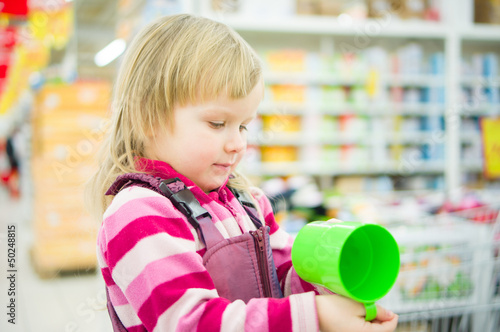 Adorable girl on shopping cart with green cup in supermarket