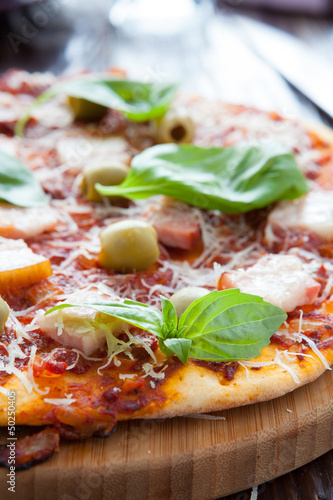 thin pizza with bacon, olives and basil on board