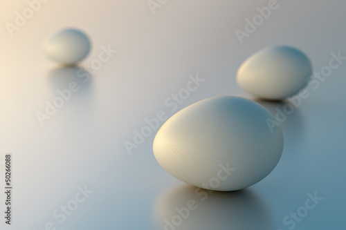 Three hen's eggs on a silver reflecting surface