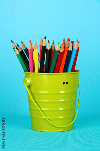 Colorful pencils in pail on blue background