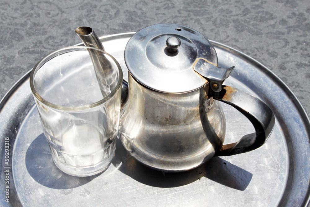 A kettle with a empty tea glass on a tray