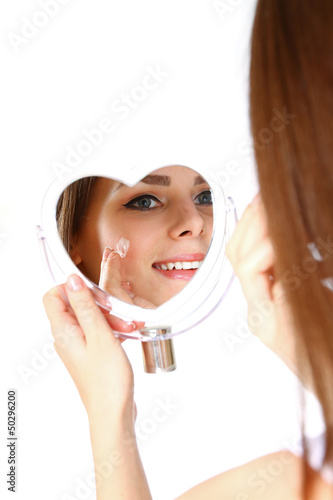 Beautiful woman applying cream on face on white background