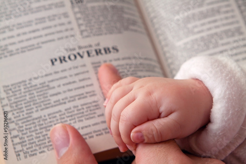 Obraz na plátně Baby Holding Dad’s Finger on Bible