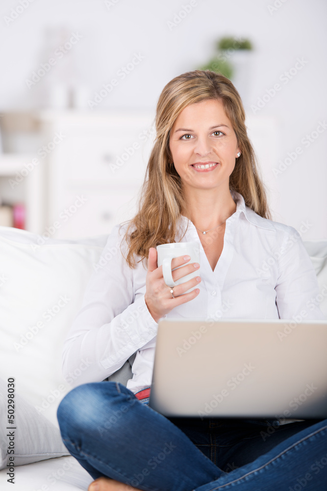 frau sitzt mit kaffee und laptop auf dem sofa frau sitzt mit kaffee und laptop auf dem sofa