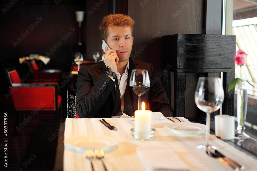 Serious young man in suit at a restaurant talking on phone