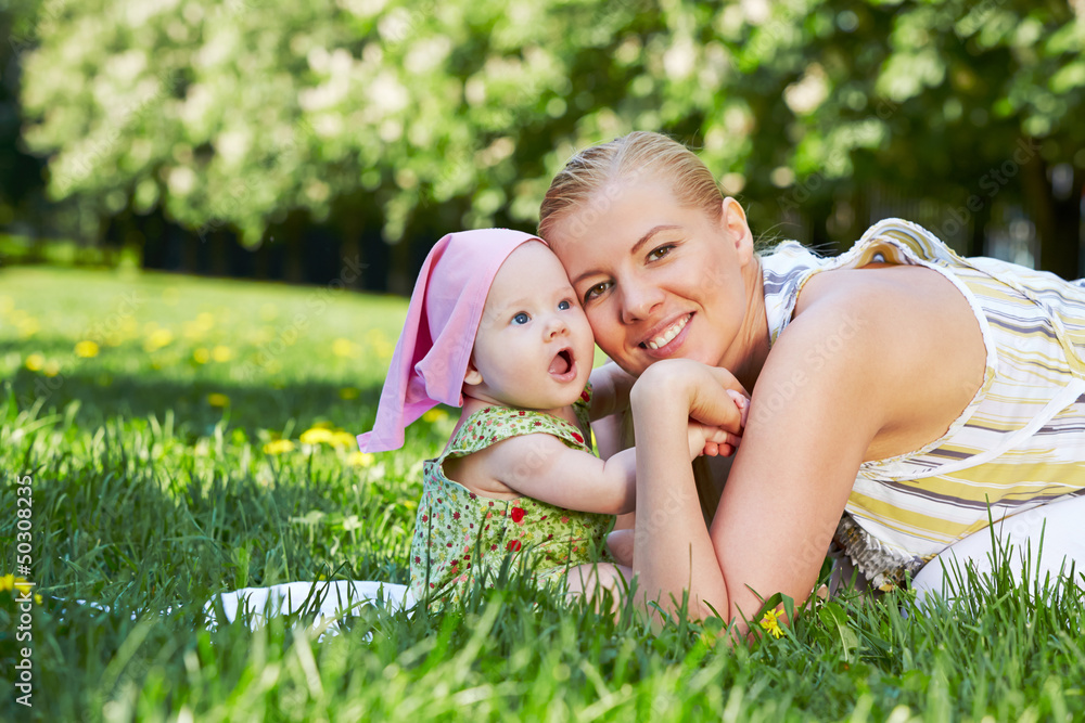 Young mother and her baby snuggle their cheeks, sitting on grass Young mother and her baby snuggle their cheeks, sitting on grass