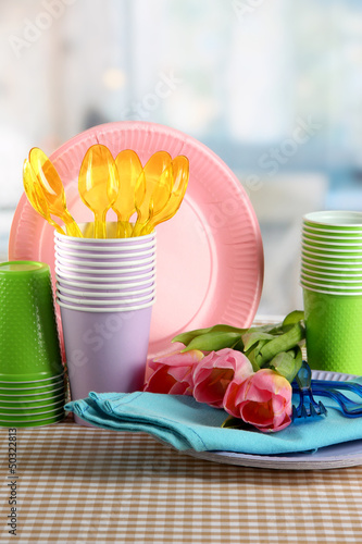 Fototapeta Naklejka Na Ścianę i Meble -  Multicolored plastic tableware on table with tulips close up