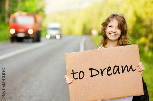 Young tourist hitchhiking along a road with message board