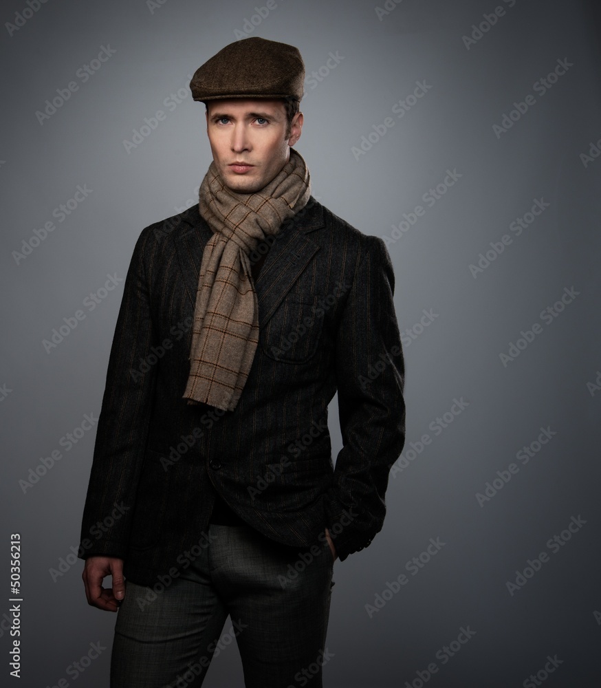 Young man in brown jacket wearing cap and scarf isolated on grey Young man in brown jacket wearing cap and scarf isolated on grey