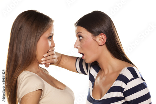 one girl silencing her mate with a hand on her mouth