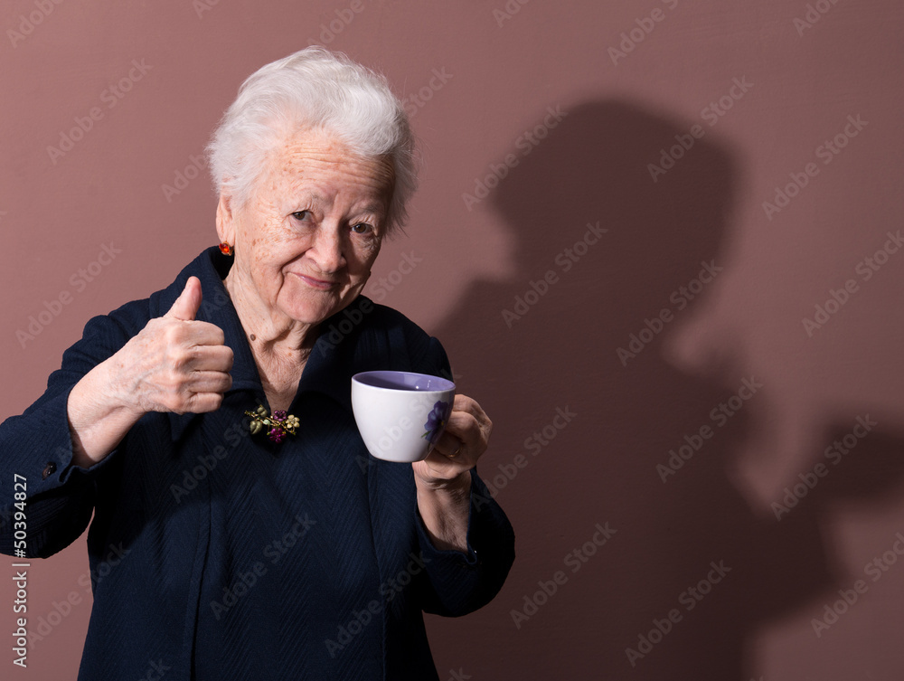 © vbaleha - Old woman enjoying coffee or tea cup over brown background