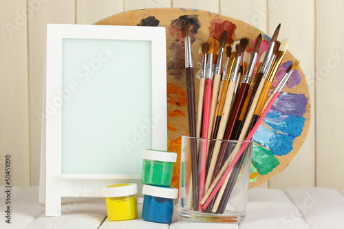 Photo frame as easel with artist's tools on wooden background