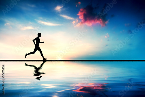 Silhouette of man running at sunset. Water reflection