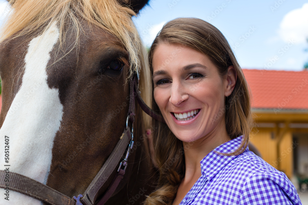 Obraz premium Young woman in the stable with horse in sunshine