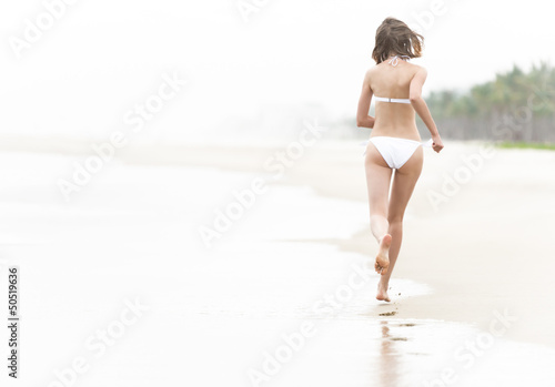 Pretty woman running on wet sand along beach.