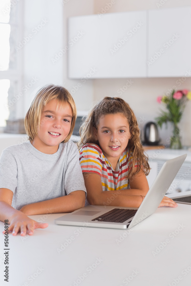 Two children looking at the camera with laptop in front Two children looking at the camera with laptop in front