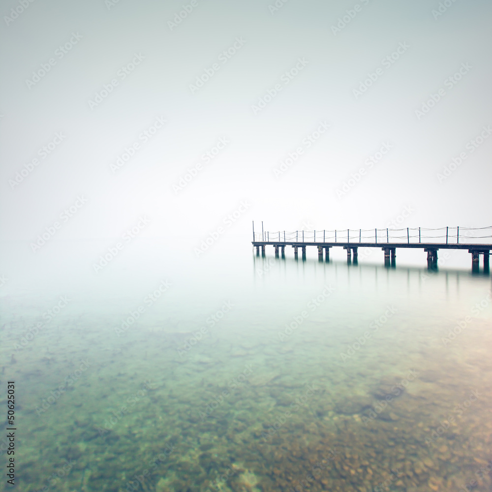 Pier or jetty silhouette in a foggy lake. Garda lake, Italy