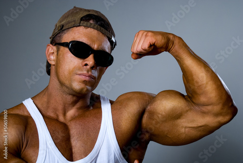 A strong man shows his muscles. Trained body. The gray backgroun