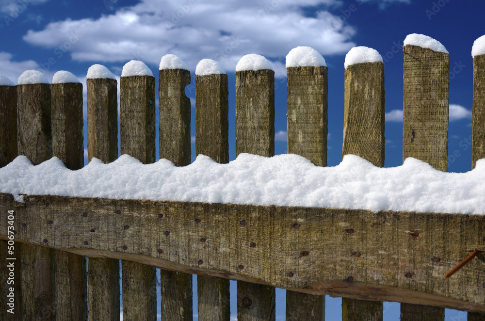 Schneebedeckter Holzzaun vor blauem Wolkenhimmel Schneebedeckter Holzzaun vor blauem Wolkenhimmel