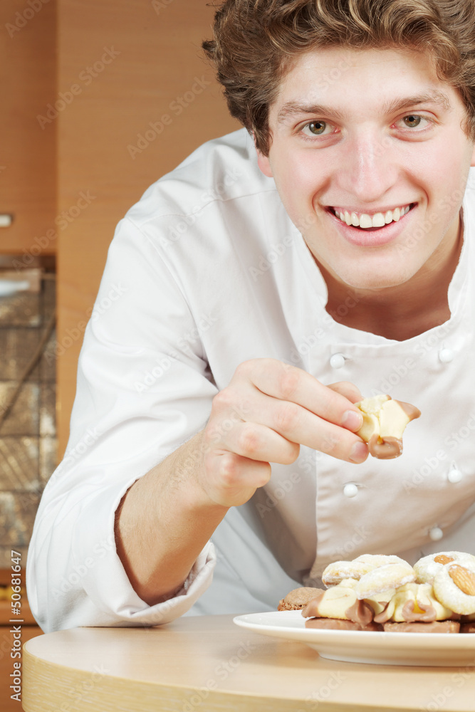 Young smiling confectioner lays out cookies and cakes on plate Young smiling confectioner lays out cookies and cakes on plate