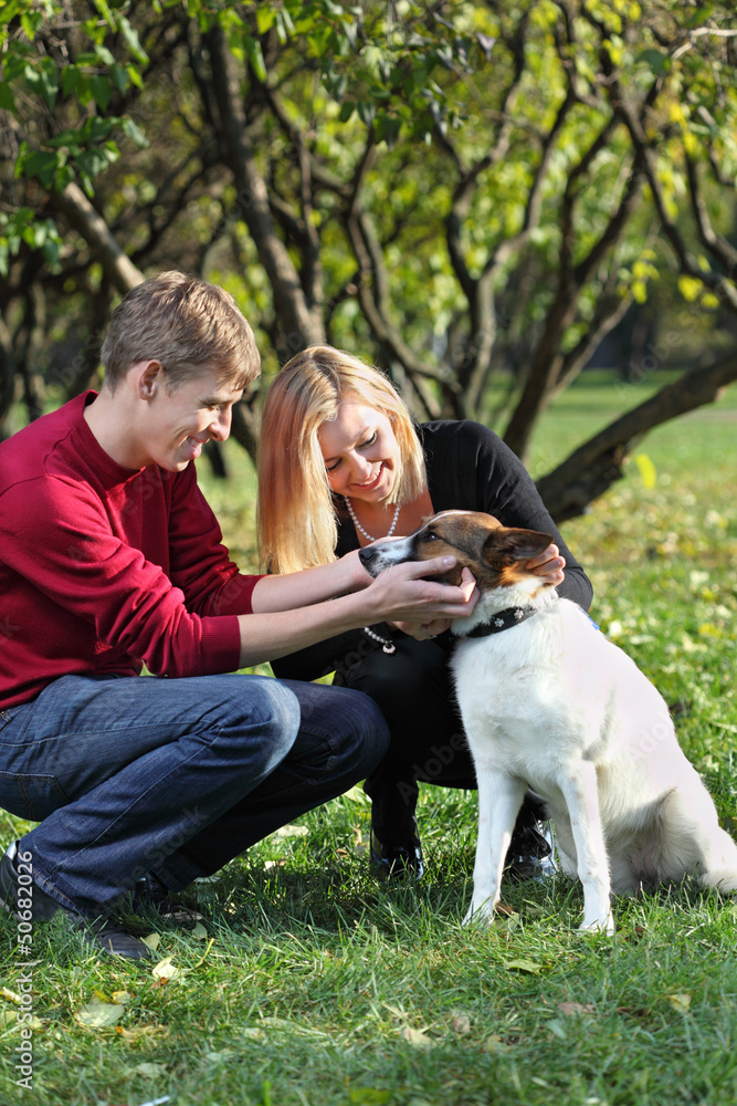 Happy couple smile and touch dog in park at sunny autumn day. Happy couple smile and touch dog in park at sunny autumn day.