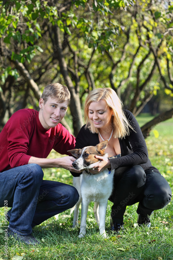 Happy couple squat and touch dog in park at sunny autumn day. Happy couple squat and touch dog in park at sunny autumn day.