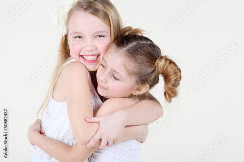 Two little smiling girl in clean white clothes hugged strongly.