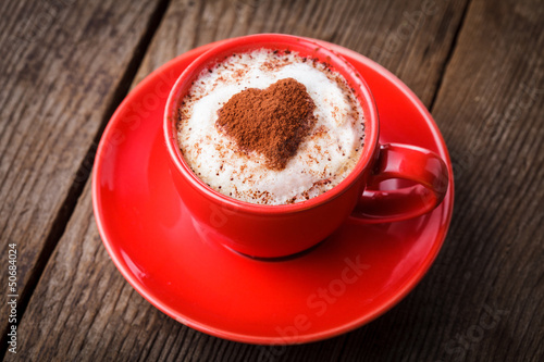 Red cup with cappuccino and heart decoration over foam. 