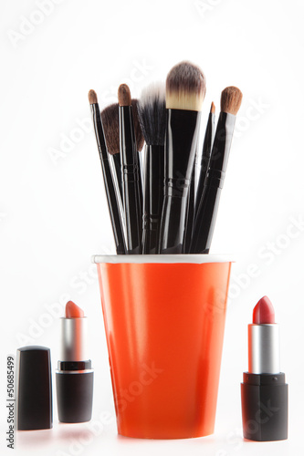 Cosmetic brushes in orange cup and lipsticks