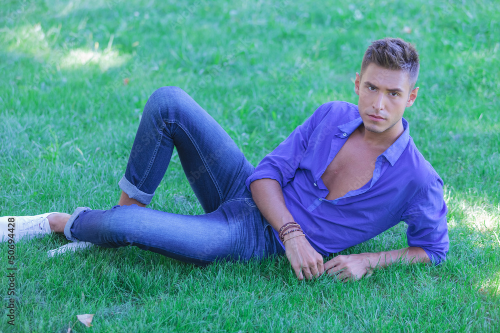 serious young man resting in grass serious young man resting in grass