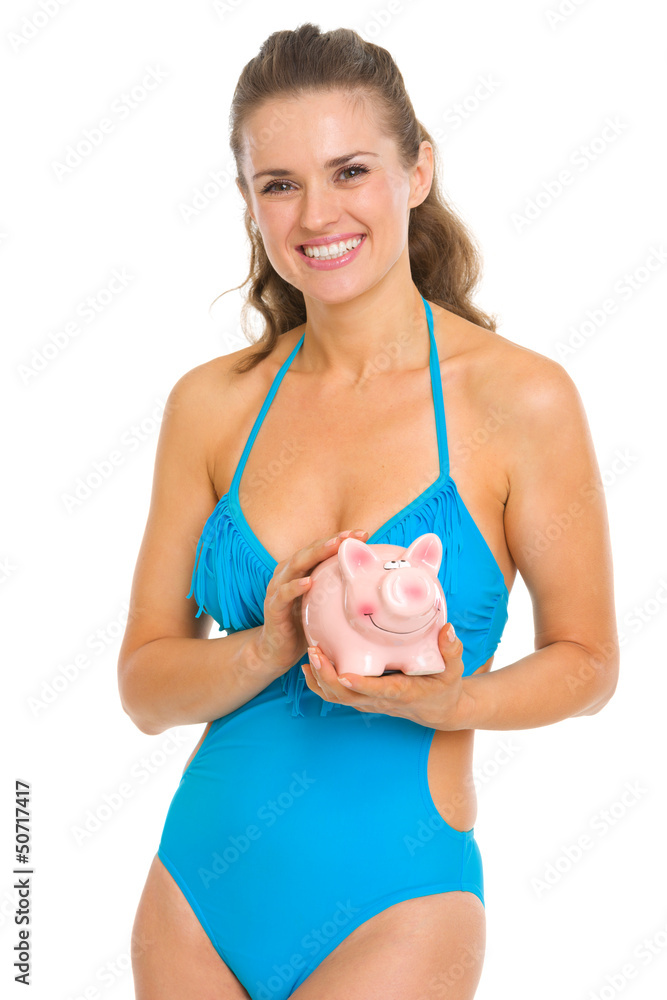 Smiling young woman in swimsuit holding piggy bank Smiling young woman in swimsuit holding piggy bank