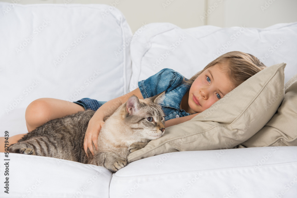 Little girl laying on sofa with her tabby cat Little girl laying on sofa with her tabby cat
