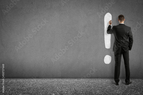 businessman painting exclamation mark on wall