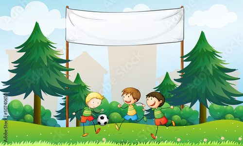 Three boys playing soccer below an empty banner