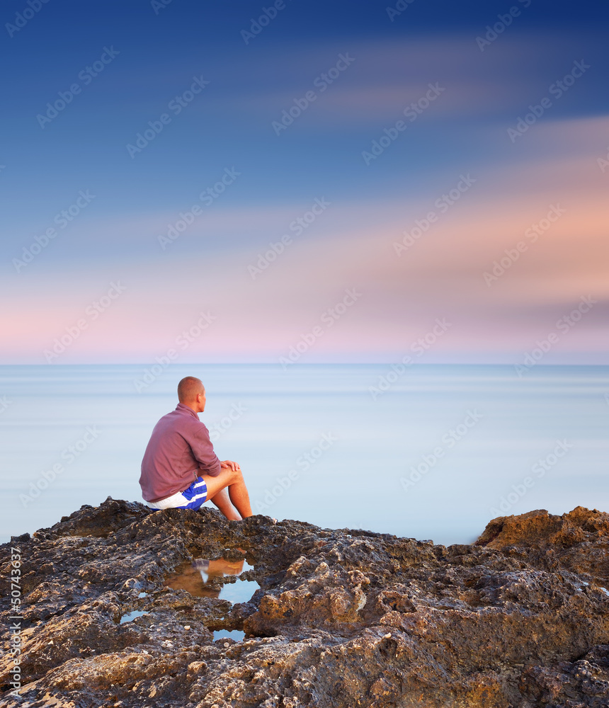 Man sitting on a rock by the sea Man sitting on a rock by the sea