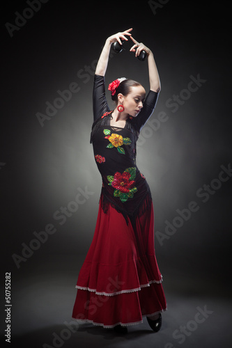 young woman dancing flamenco with castanets on black