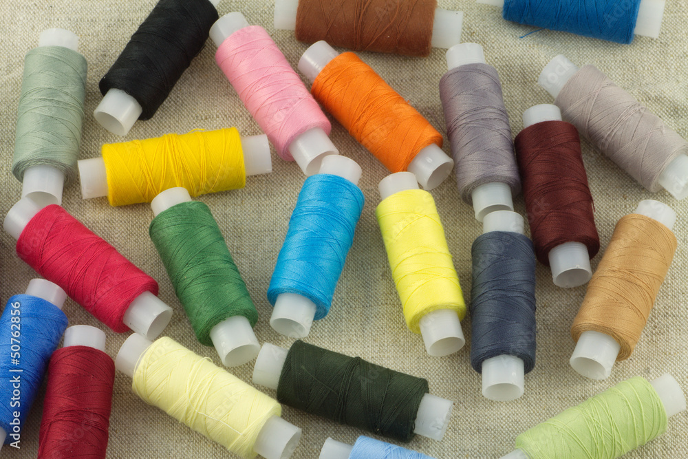 Lot of colored thread spools on beige fabric close up Lot of colored thread spools on beige fabric close up