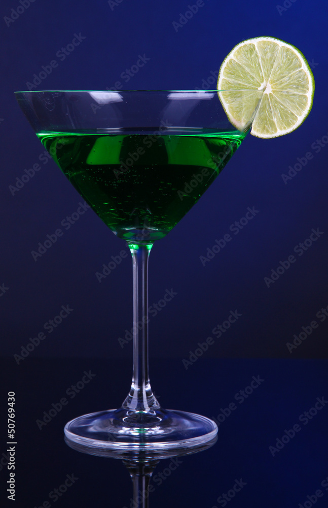 Green cocktail in martini glass on dark blue background
