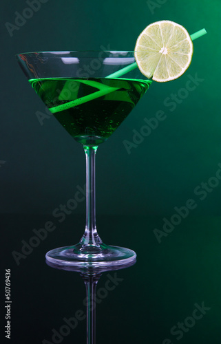 Green cocktail in martini glass on dark green background