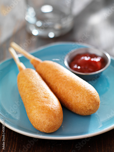 two corn dogs on a plate with ketchup