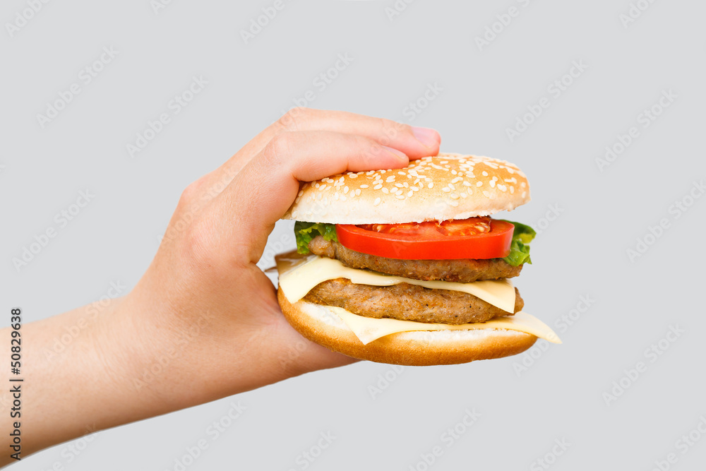 Hand holding delicious fast food cheeseburger on grey background Hand holding delicious fast food cheeseburger on grey background