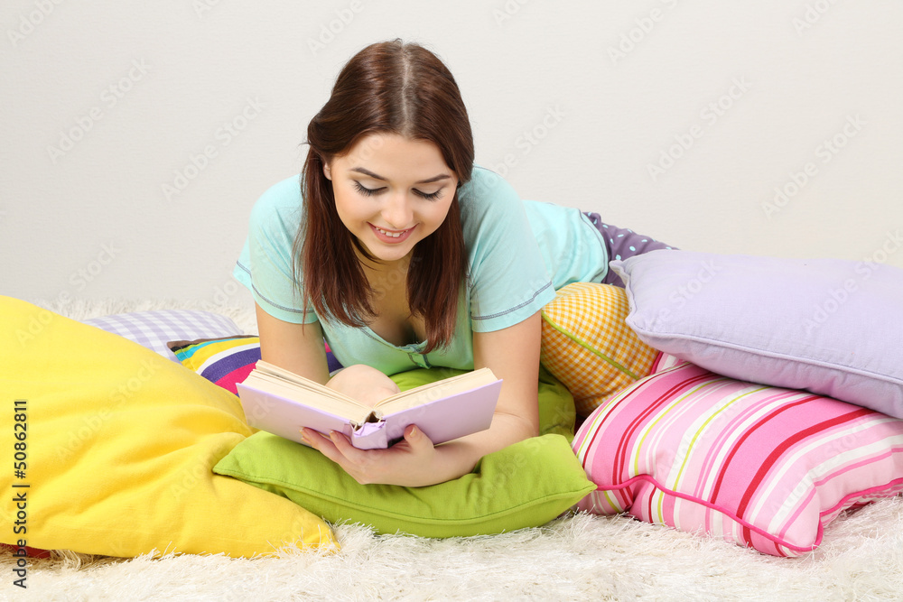 Beautiful young girl with pillows and book in room Beautiful young girl with pillows and book in room